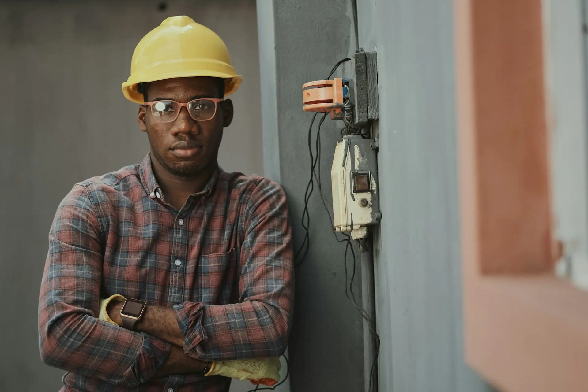 An electrician in a yellow hard hat, arms folded, in a house being rewired
